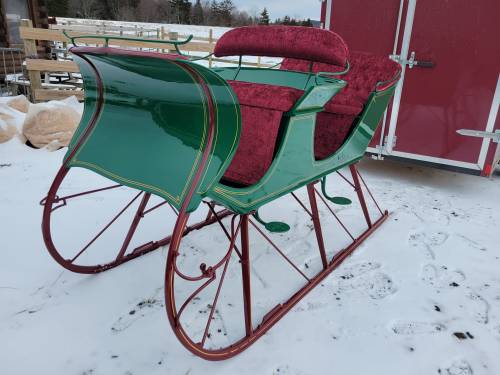 A vintage green and red sleigh with plush upholstery, resting on a snowy surface.