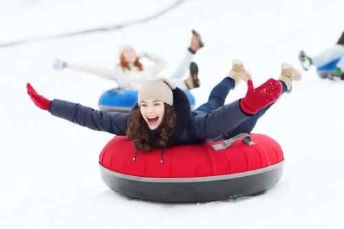 A joyful girl in a red snow tube, arms outstretched, sliding down a snowy hill with friends in the background.