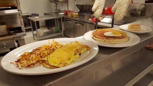 A breakfast spread featuring an omelette, hash browns, a pancake with an egg, and a biscuit on white plates.