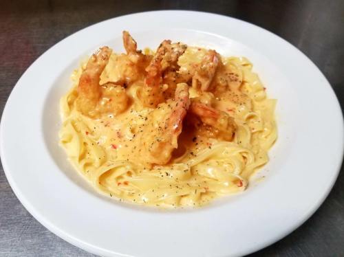 Creamy fettuccine pasta topped with shrimp in a rich sauce, garnished with black pepper, served on a white plate.