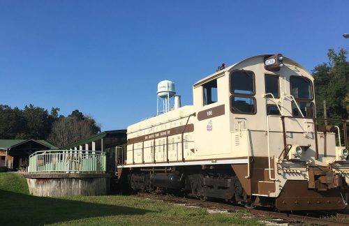 A vintage train engine parked near a wooden platform and a water tower under a clear blue sky.