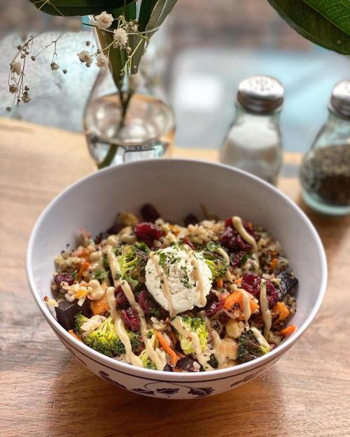 A colorful salad bowl with quinoa, broccoli, carrots, and a dollop of cream, garnished with herbs.