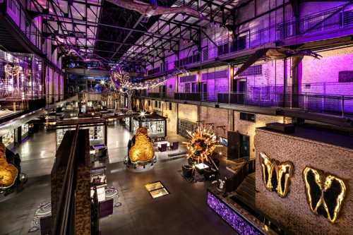 A spacious, modern museum interior with vibrant lighting, showcasing large sculptures and exhibits in an industrial setting.