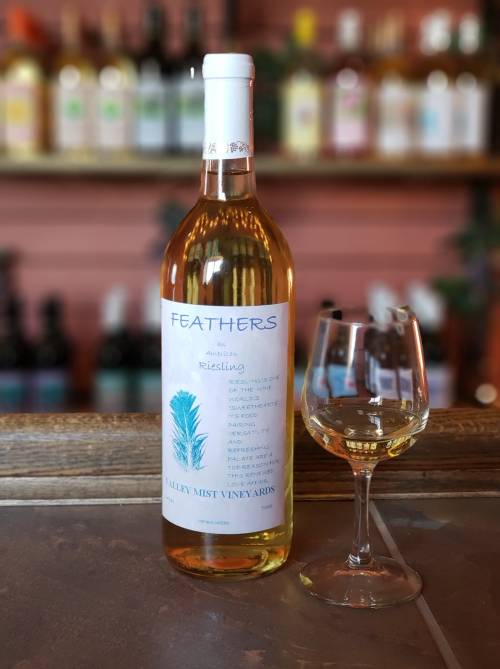 A bottle of Feathers Riesling wine next to a filled glass, set against a blurred background of wine bottles.