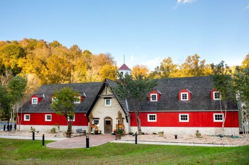 A red barn with a stone base, surrounded by trees and autumn foliage, set against a clear blue sky.