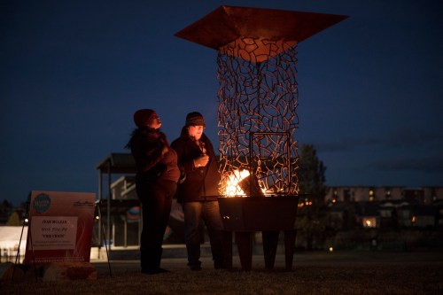 Two people stand by a modern fire pit at dusk, enjoying the warmth and ambiance of the flames.