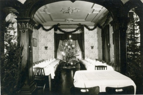 A vintage dining room decorated for the holidays, featuring a Christmas tree and festive garlands.