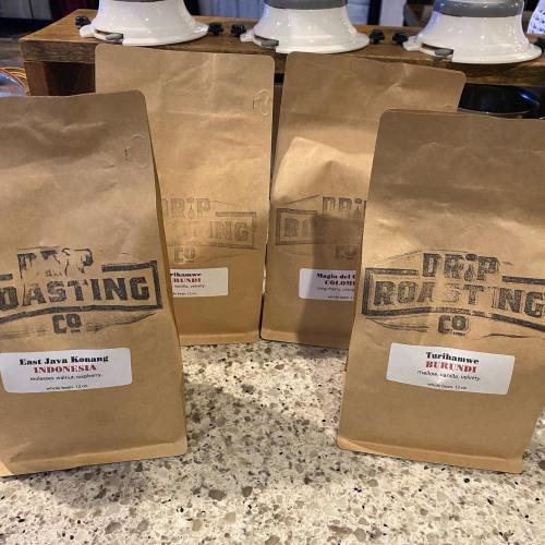 Three brown coffee bags labeled with their origins: East Java, Burundi, and Colombia, displayed on a countertop.