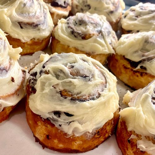 Freshly baked cinnamon rolls topped with creamy frosting, arranged neatly on a tray.