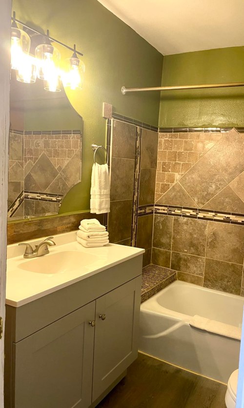 A modern bathroom featuring a tub, tiled walls, a sink with storage, and decorative lighting.