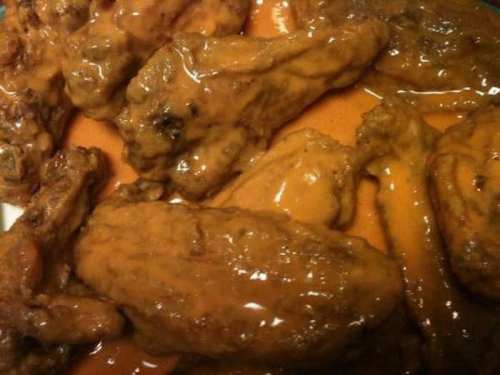 A close-up of chicken wings coated in a rich, orange sauce, arranged on a plate.