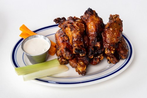 A plate of grilled chicken wings with a side of ranch dressing, celery, and carrot sticks.