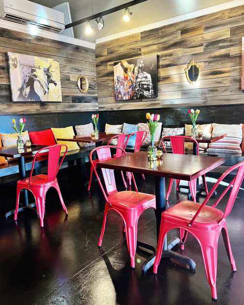 Cozy café interior with wooden walls, colorful cushions, red chairs, and flower vases on tables.
