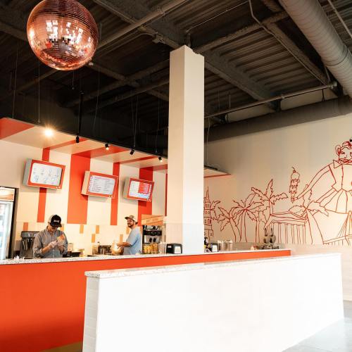 A modern café interior with red and white walls, two baristas working behind the counter, and a disco ball overhead.