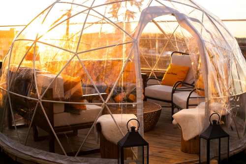 A cozy, transparent igloo structure with seating, illuminated by warm sunset light on a rooftop.