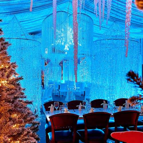 A beautifully decorated dining area with blue lighting, shimmering curtains, and a festive tree in the foreground.