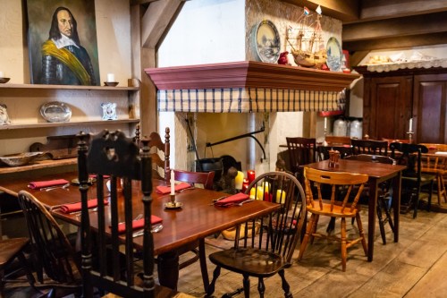 Cozy restaurant interior with wooden tables, chairs, and a fireplace, featuring nautical decor and a portrait on the wall.