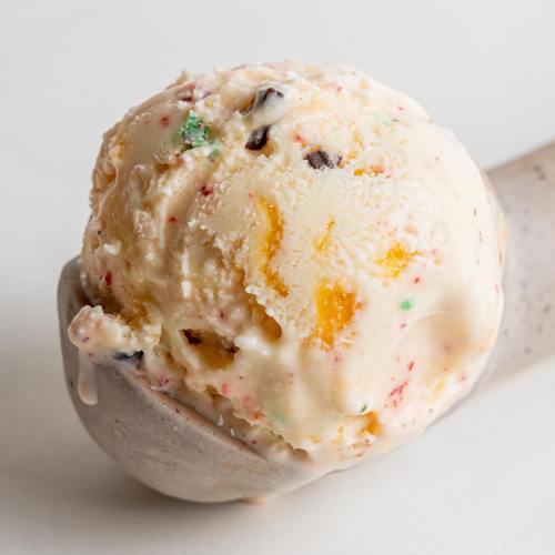 A scoop of colorful ice cream with chunks of fruit and chocolate, resting in a gray ceramic dish.