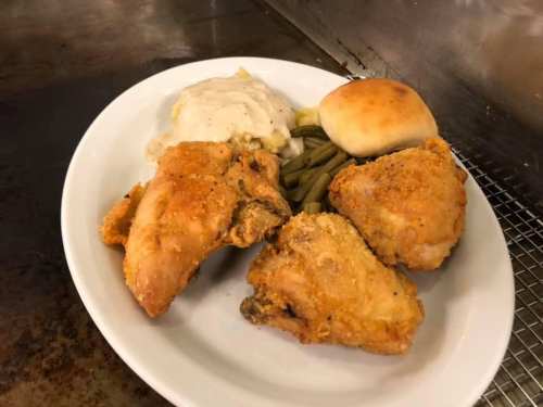 A plate of fried chicken, mashed potatoes with gravy, green beans, and a dinner roll.