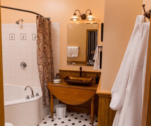 A cozy bathroom featuring a bathtub, a wooden sink, a mirror, and a shower curtain with a decorative pattern.