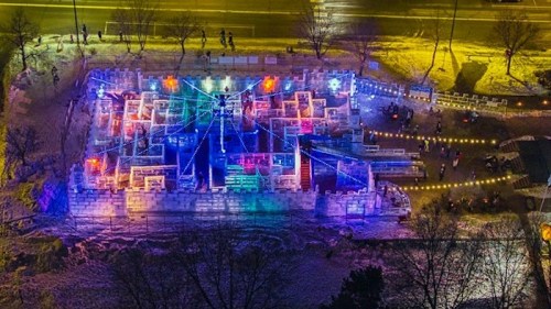 Aerial view of a colorful ice maze illuminated with lights, surrounded by snow and trees at night.