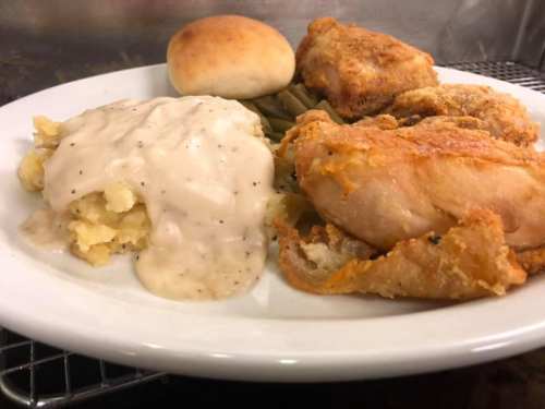 A plate of fried chicken, creamy mashed potatoes with gravy, green beans, and a roll.
