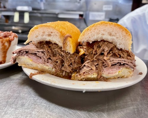 A close-up of a sandwich filled with shredded beef on a soft bun, served on a plate.