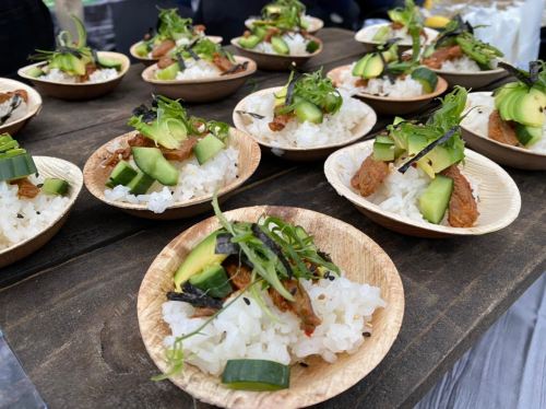 A close-up of small wooden bowls filled with rice, topped with cucumber, greens, and garnishes, arranged on a table.
