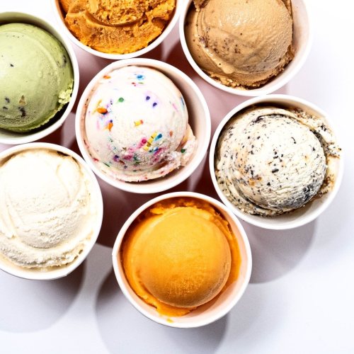 A variety of ice cream scoops in cups, including green, orange, brown, and white flavors, arranged in a circle.