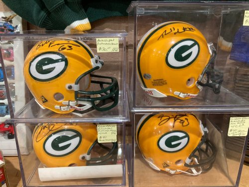 Four signed Green Bay Packers helmets displayed in clear cases, showcasing team colors and logos.