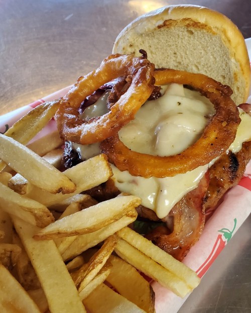A grilled chicken sandwich topped with onion rings and creamy sauce, served with a side of golden fries.