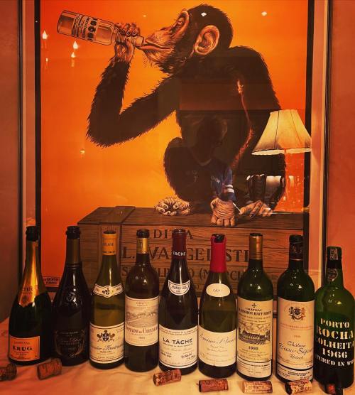 A playful chimpanzee poster behind a lineup of wine bottles and champagne, with corks scattered on the surface.