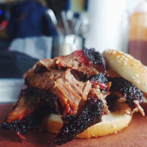 Close-up of a juicy brisket sandwich with a sesame seed bun, showcasing tender meat and a smoky crust.