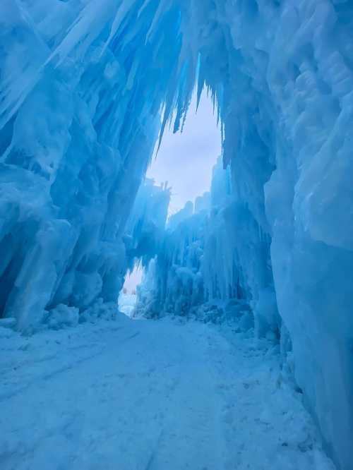 A stunning ice cave with towering blue icicles and a narrow pathway leading through the frozen landscape.