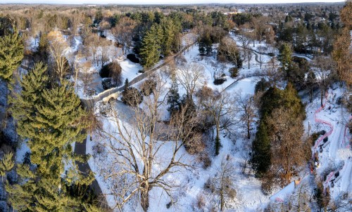 Aerial view of a snowy landscape with trees, a bridge, and a winding path in a park setting.