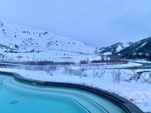 A serene winter landscape featuring a snowy mountain view and a partially frozen pool in the foreground.