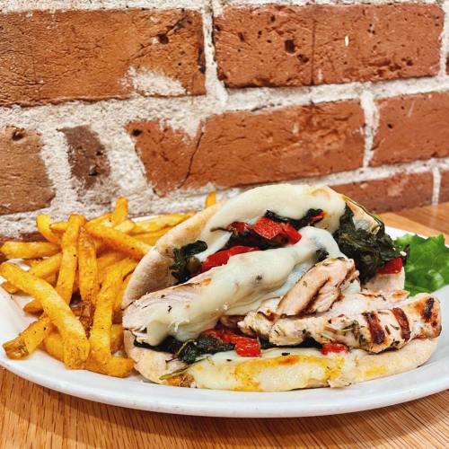 A grilled chicken sandwich with melted cheese, spinach, and red peppers, served with a side of golden fries.