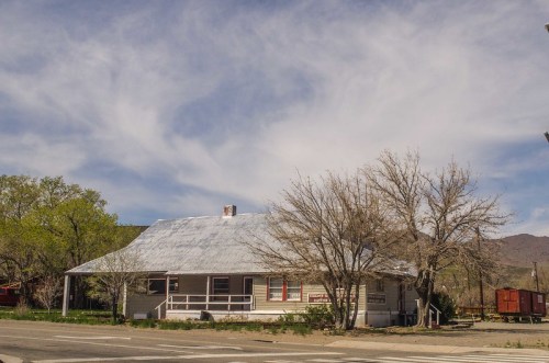 A quaint, single-story house with a metal roof, surrounded by bare trees and a clear blue sky with wispy clouds.