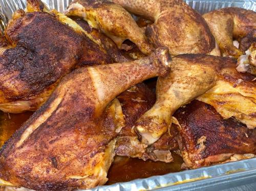 A close-up of seasoned, roasted chicken pieces in a large aluminum tray.