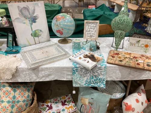 A table display featuring decorative items like a globe, framed art, and colorful textiles in a market setting.