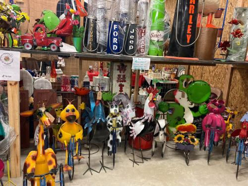 A collection of colorful metal yard art figures, including animals and vintage gas pumps, displayed in a rustic setting.