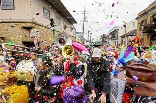 A lively street scene with a brass band, colorful costumes, and confetti during a festive parade celebration.
