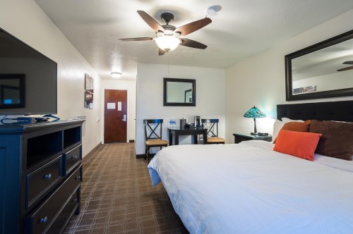 A cozy hotel room featuring a bed, dresser, TV, and a small dining area with a table and chairs.