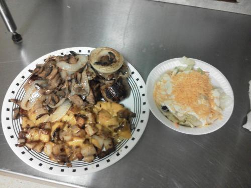 A plate of grilled meat with onions and cheese-covered potatoes, alongside a salad with shredded cheese.