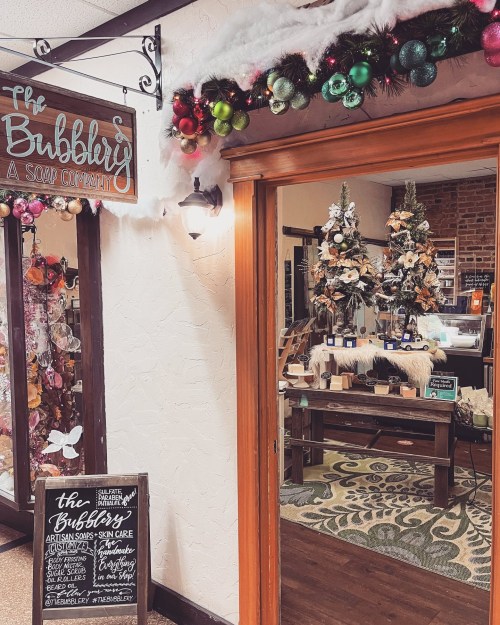 Entrance to The Bubbly, a soap company, decorated with festive ornaments and greenery, showcasing artisan products inside.