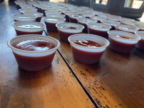 Rows of small cups filled with a reddish-brown sauce on a wooden table.