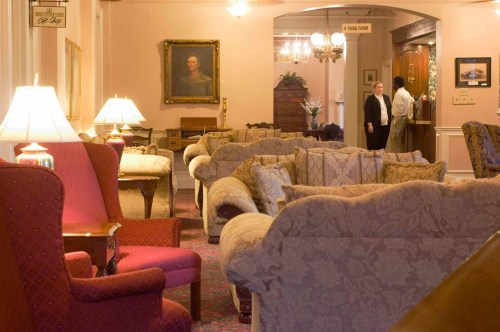 A cozy hotel lobby with plush seating, warm lighting, and a staff member attending to guests in the background.