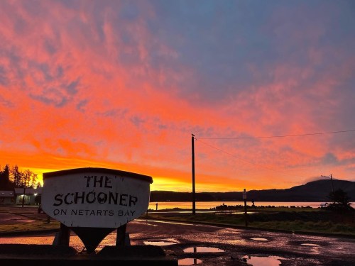 A vibrant sunset over Netarts Bay, with a sign for "The Schooner" in the foreground.