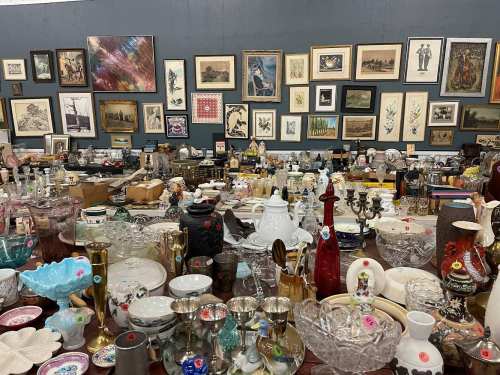 A cluttered antique shop filled with various vintage items, including glassware, artwork, and decorative pieces.