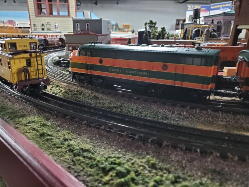 A model train set featuring a Great Northern locomotive and a yellow caboose on curved tracks in a detailed landscape.